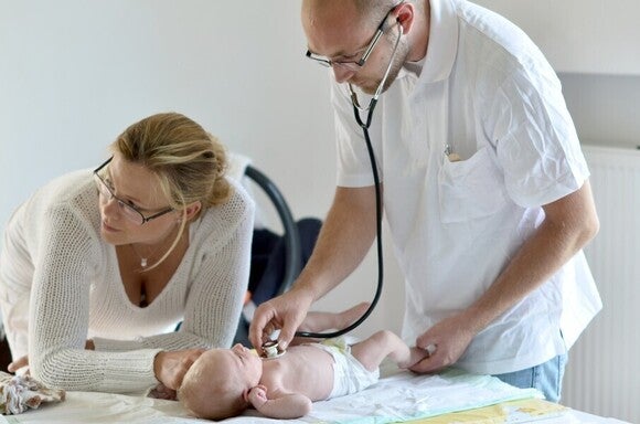 Baby wird vom Arzt untersucht, während die Mutter aufmerksam zuschaut