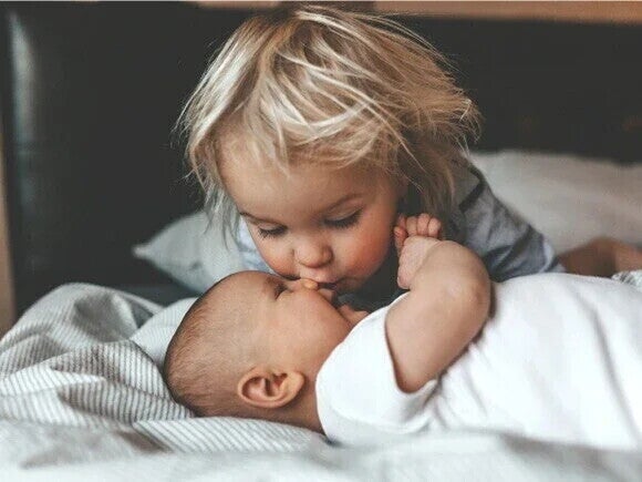 Harmonie für das Geschwister-Team: Ein älteres Kind gibt seinem Baby-Geschwisterchen einen Kuss.