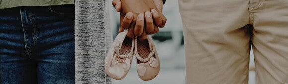 Paar mit Kinderwunsch hält sich an den Händen und dabei zugleich kleine Kinderschuhe