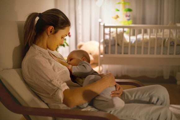 Baby liegt nachts an Brust der Mutter und wird gestillt