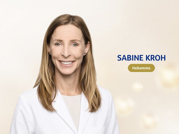 Porträtfoto einer lächelnden Frau im weißen Arztkittel vor einem weichen goldenen Bokeh-Hintergrund, freundlich und professionell wirkend.
