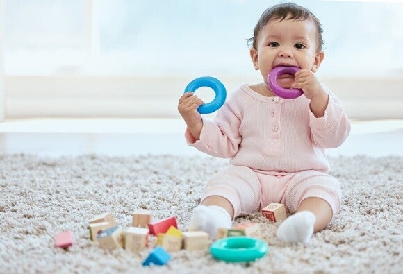 Ein Baby spielt mit Ringen und Holzklötzen auf einem Teppich