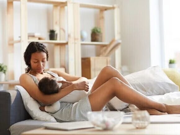 Eine Mutter liegt mit ihrem Baby beim Clusterfeeding gemütlich auf der Couch Eine Mutter liegt mit ihrem Baby beim Clusterfeeding gemütlich auf der Couch