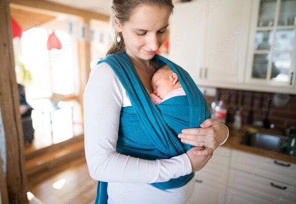 Eine Mutter hält ihr schlafendes Baby in einem Wickel vor ihrer Brust Eine Mutter hält ihr schlafendes Baby in einem Wickel vor ihrer Brust