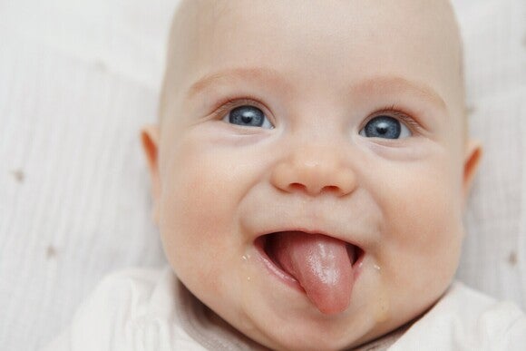 Baby mit blauen Augen lächelt und streckt die Zunge raus.