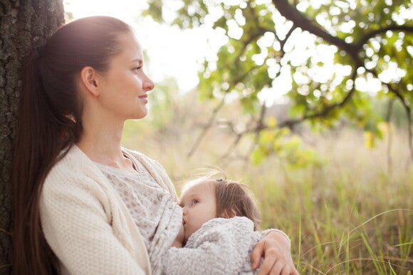 Frau stillt ihr Baby an einem Baum Frau stillt ihr Baby an einem Baum