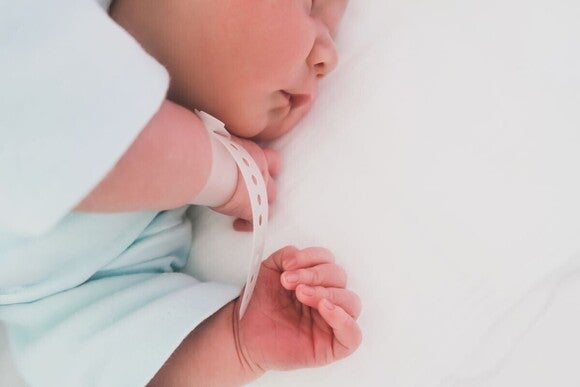 Frisch geborenes Baby in einer Liege und mit Namensband am Handgelenk