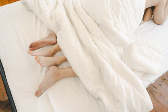 Füße eines Paares unter einer Decke symbolisieren die liebevolle Zweisamkeit, die beim Kinderwunsch wichtiger ist als bestimmte Stellungen