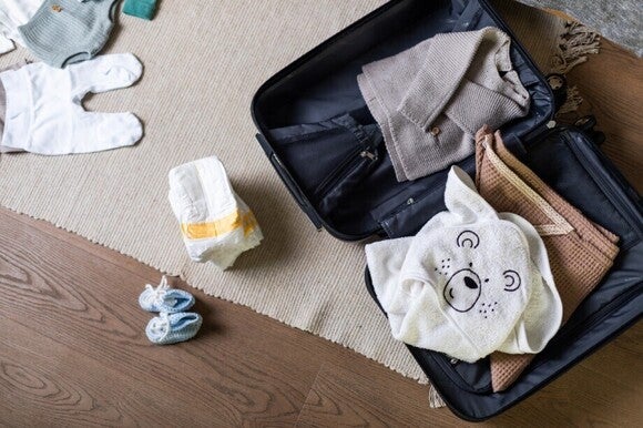 Offene Tasche mit Baby Kleidung und Windeln liegen auf dem Boden.