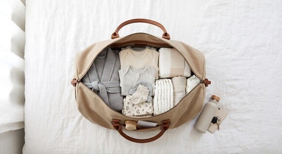 Foto einer offen gepackten Reisetasche mit gefalteter, neutraler Kleidung auf einem Bett