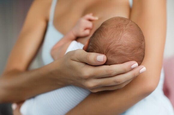 Mutter haltet den Hinterkopf ihres Babys, während sie das Baby auf dem Arm stillt.