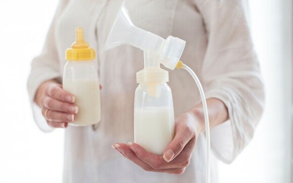 Frau haltet eine volle Milchflasche in der einen Hand und mit der anderen Hand ein Milchpump Gerät.