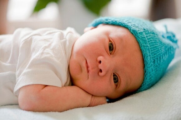Säuglings-Baby mit blauer Wollmütze auf dem Kopf liegt seitlich auf dem Bauch.