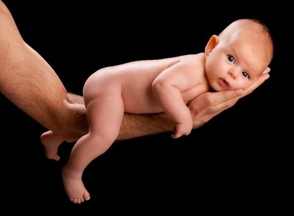 Baby liegt auf dem Arm von seinem Papa mit dem Bauch nach unten gedreht
