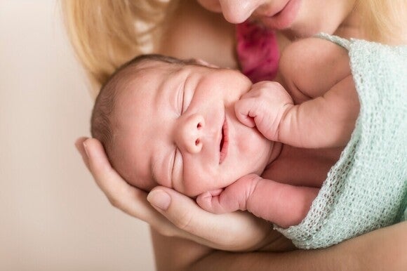 Baby liegt lächelnd in den Armen von seiner Mama