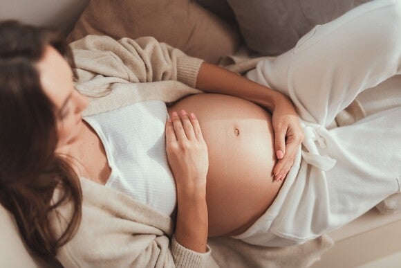 Schwangere Frau liegt entspannt auf der Seite und hält ihren Bauch.