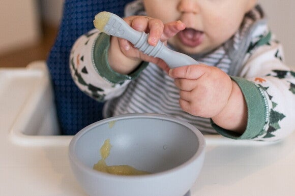 Baby hält Löffel in der Hand während es Apfelmus ist Baby hält Löffel in der Hand während es Apfelmus ist