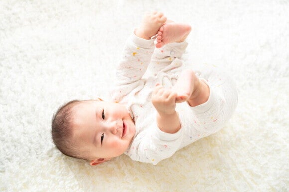 Glückliches Baby liegt auf dem Rücken und streckt mit seinen Händen nach seinen Füßen. Glückliches Baby liegt auf dem Rücken und streckt mit seinen Händen nach seinen Füßen.
