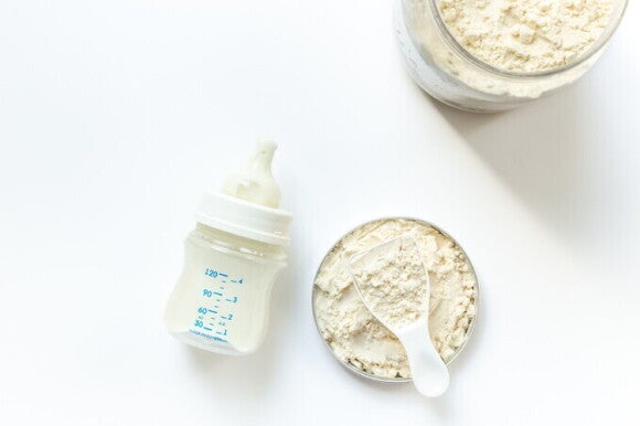 Ein Behälter mit Babymilchpulver neben einer Babyflasche, die auf die Vorbereitung für die Säuglingsernährung hinweist. Ein Behälter mit Babymilchpulver neben einer Babyflasche, die auf die Vorbereitung für die Säuglingsernährung hinweist.