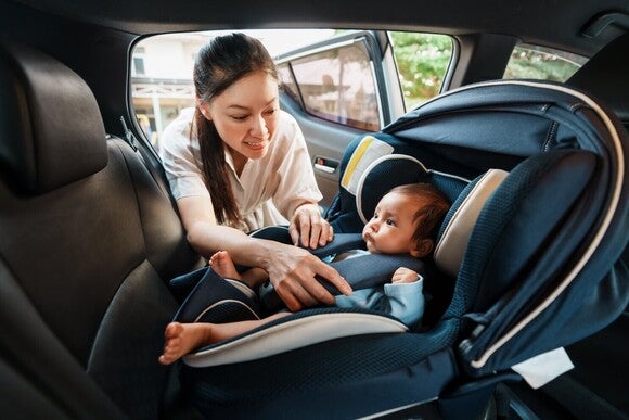 Mutter schnallt ihr kleines Baby im Kindersitz an.