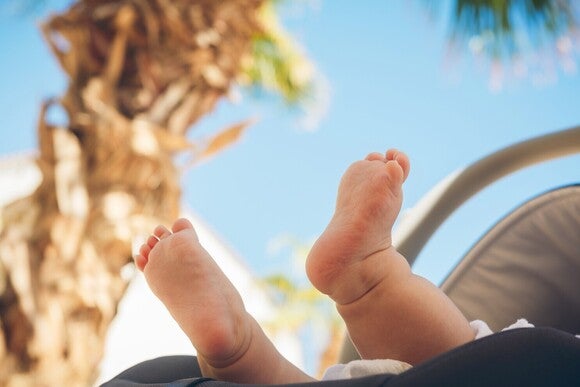 Wedelnde Babyfüße aus dem Kinderwagen und dahinter eine Palme