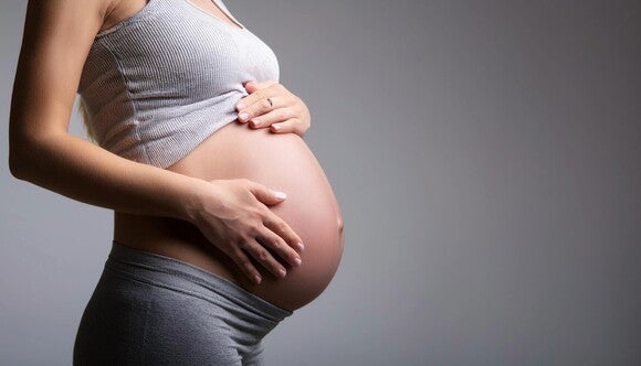 Hochschwangere Frau steht seitlich, hat ihren Bauch frei und hält ihre Hände um den Bauch.