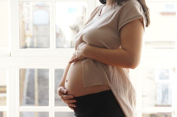 Frau hält ihren Bauch mit beiden Händen und zeigt ihren Bauch.