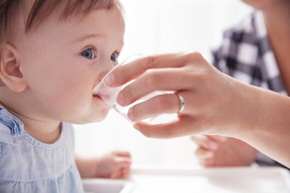 Mutter gibt ihrem Baby Wasser in einer kleinen Tasse