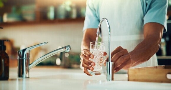 Mann füllt das Wasser in ein Glas aus einem Wasserfilterungssystem.