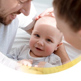 Baby lächelt in die Kamera mit seinen Eltern nebendran