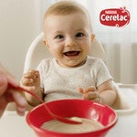 Baby in high chair with red bowl and spoon of food.