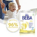Toddler held by adult, BEBA formula container in foreground.